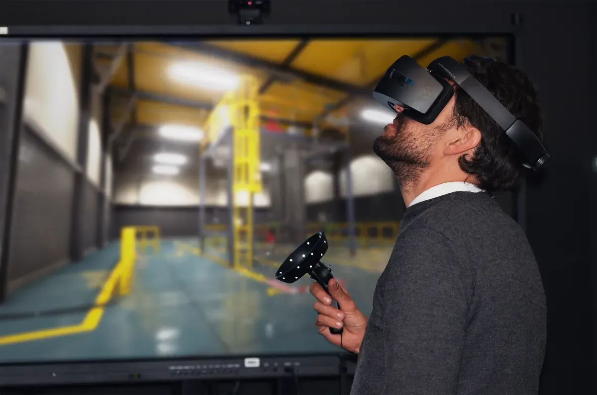 A participant using a VR headset and controllers in front of the Abilitee industrial environment.