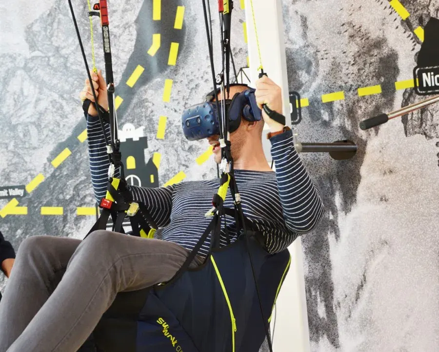 Visitor wearing a VR headset in the Technopolis paragliding harness and holding the steering handles.